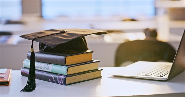 Graduation cap, books and laptop on a desk