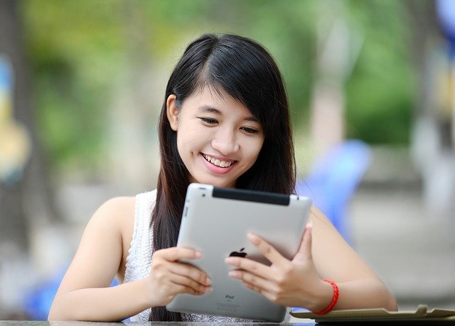 Smiling student sitting outdoors using a tablet.