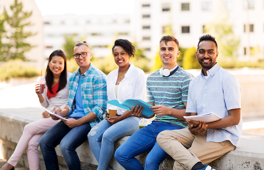 A diverse group of five students sitting side by side, smiling with study materials in hand.
