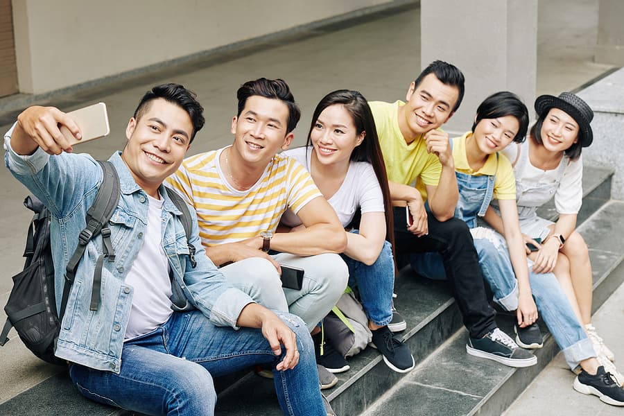 Vietnamese students sitting on the steps of a university taking a selfie