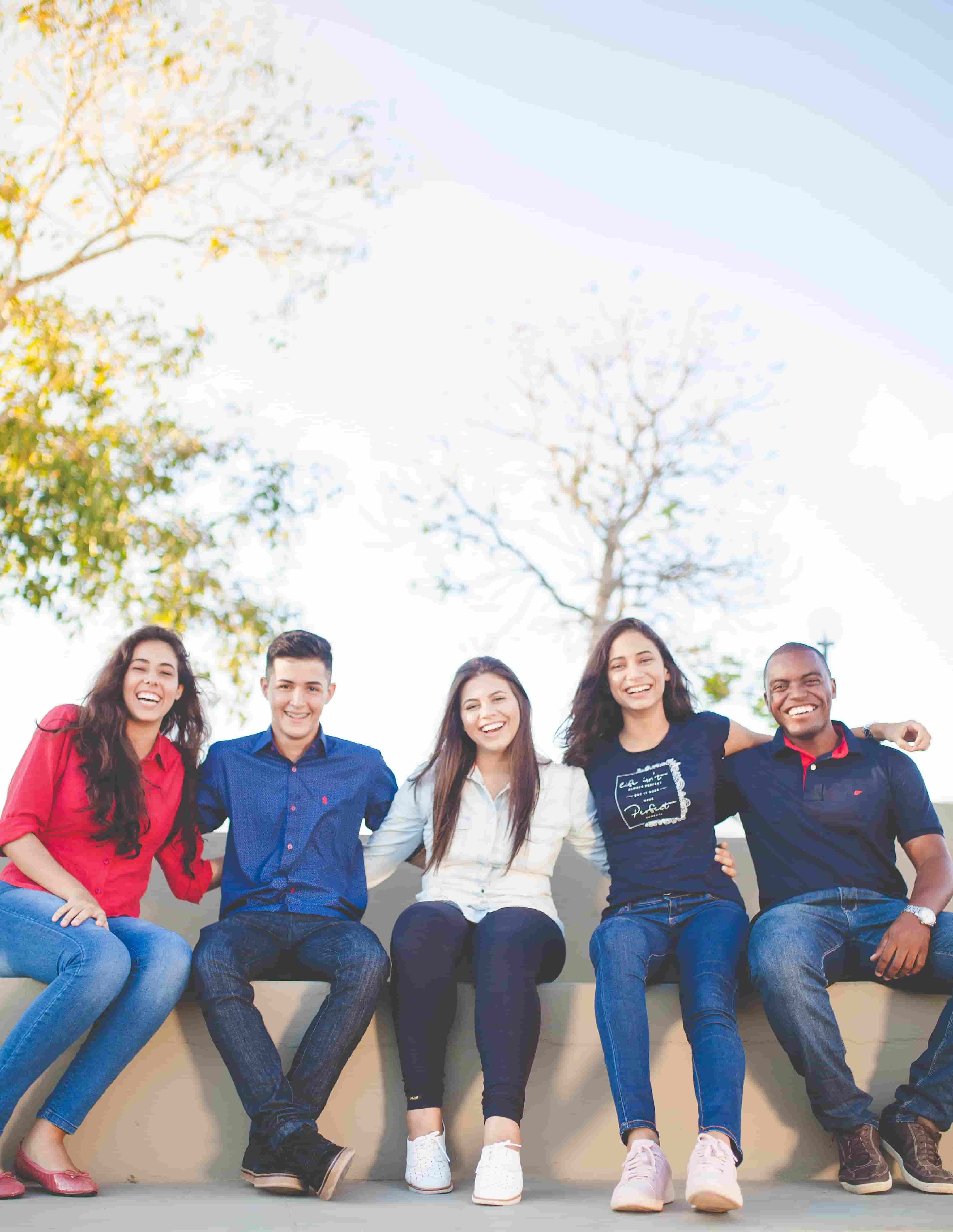 A group of five cheerful international students sitting together, laughing and bonding on a sunny day.