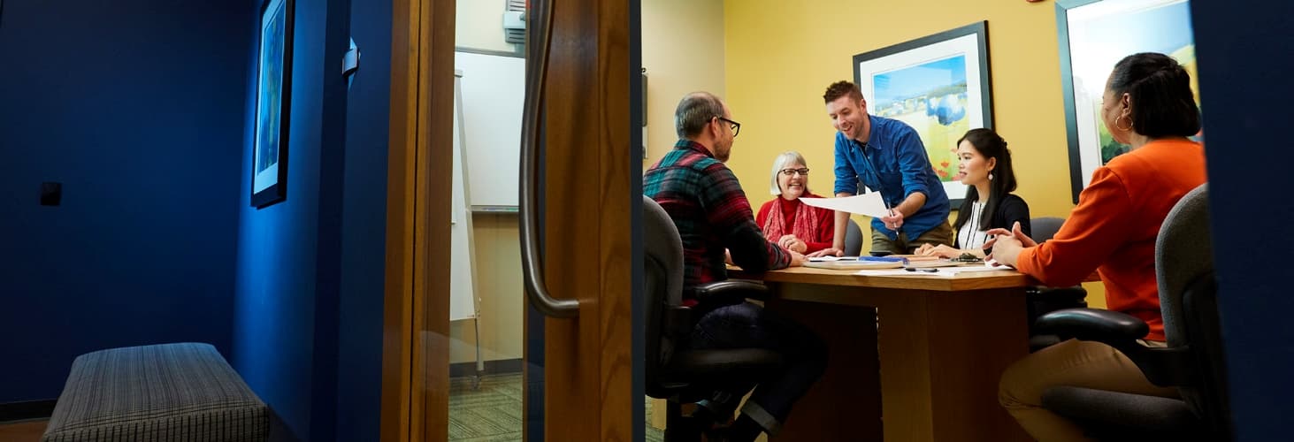 Five individuals discussing documents within a conference room.