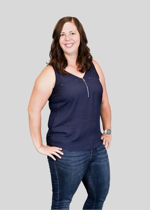 Amy Kawa stands with a friendly smile, wearing a sleeveless navy top and denim jeans.