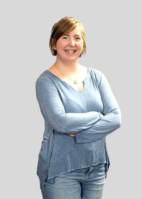 Ashley Johnson stands with arms crossed, sporting a comfortable blue top and a cheerful smile.