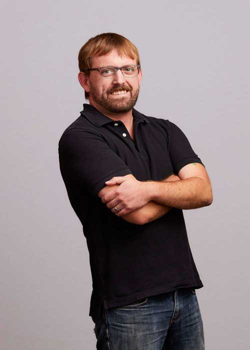 Chris Conard with arms crossed, wearing glasses and a black polo shirt.