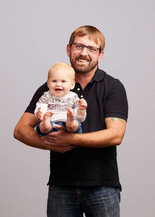 Chris Conard holding a smiling baby, both enjoying the moment.