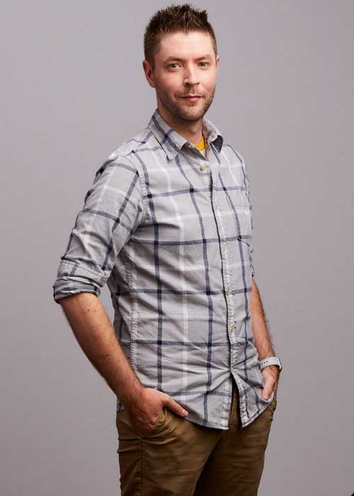 David Jarvela poses with hands in pockets, wearing a plaid shirt and khaki pants.