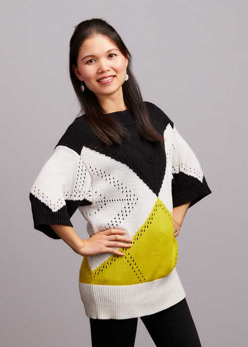 Jade Jiang Rieger posing with her hand on her hip, wearing a stylish black, white, and yellow sweater.
