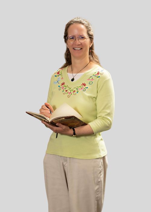 Karen Krug engaged in reading an old book, wearing a pastel yellow top with floral embroidery.
