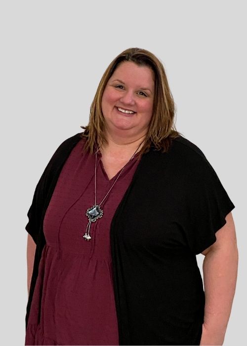 Kimberly Hajec in a black cardigan over a maroon dress, accessorized with a unique necklace.