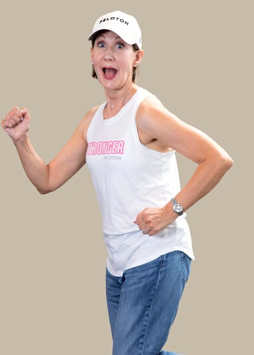Leigh Lane Peine in a playful running pose, wearing a white 'Stronger Peloton' tank top, jeans, and a cap.