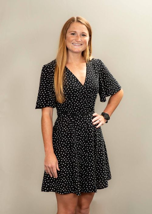 Madison Majors stands confidently in a chic black dress with white polka dots, her hands resting on her hips.