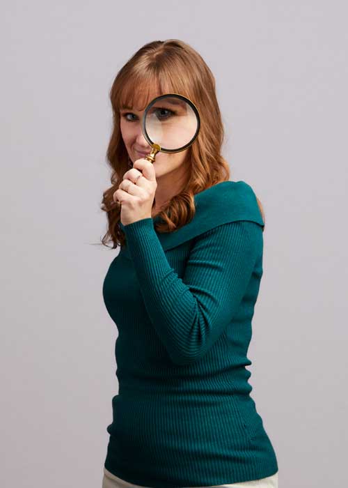 Majka Drewitz having fun looking through a magnifying glass, with a teal sweater.