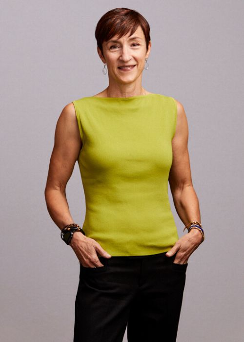 Margaret Wenger in a green sleeveless top and black pants, hands on hips with a confident stance.