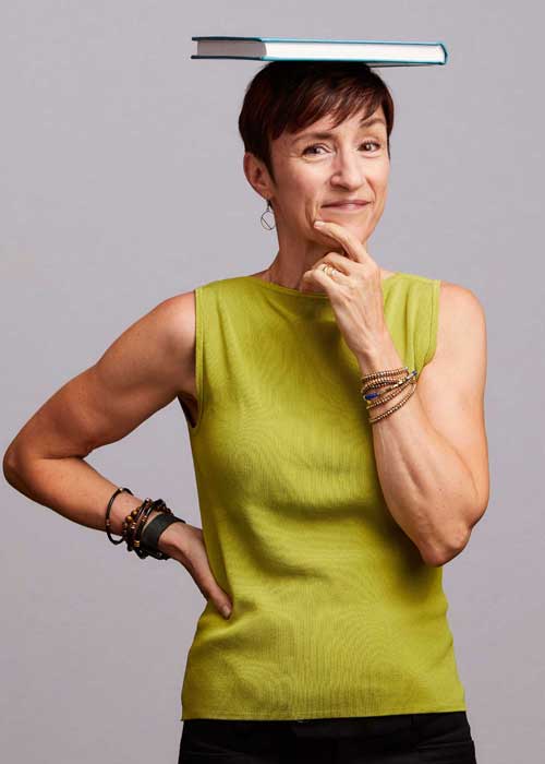 Margaret Wenger with a thoughtful pose, balancing a blue book on her head, wearing a lime green sleeveless top.