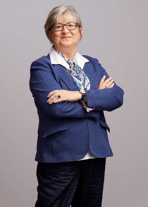 Marybeth Gruenewald with arms crossed, sporting a blue blazer and a patterned scarf.