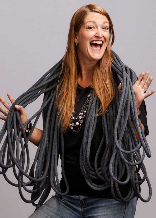 Melissa Ganiere laughing joyously, entangled in a mass of gray networking cables, sporting a black top and a necklace.
