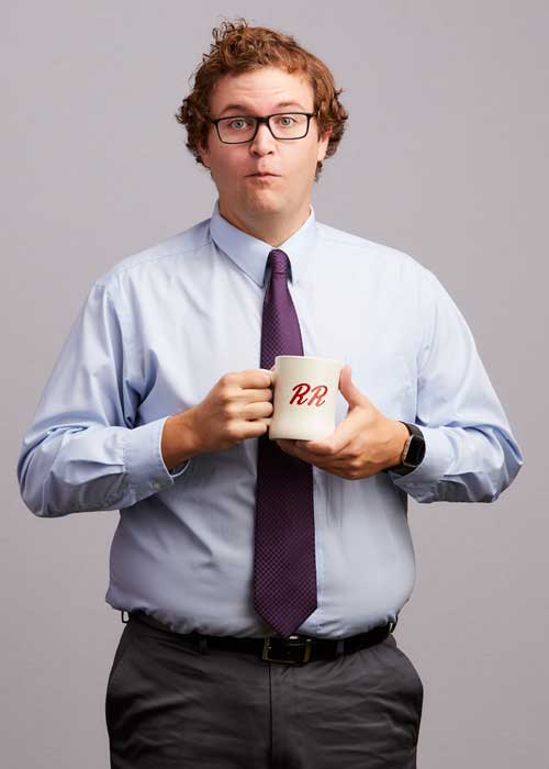Nick Kelley with an amusing expression, clutching a white mug with 'RR' on it, in a light blue dress shirt and burgundy tie