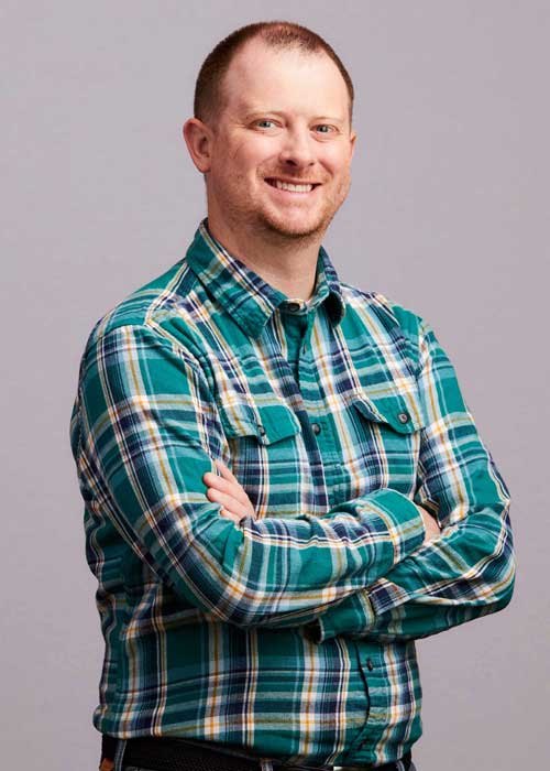 Timothy Kell with a friendly smile, arms crossed, dressed in a green and blue plaid shirt.