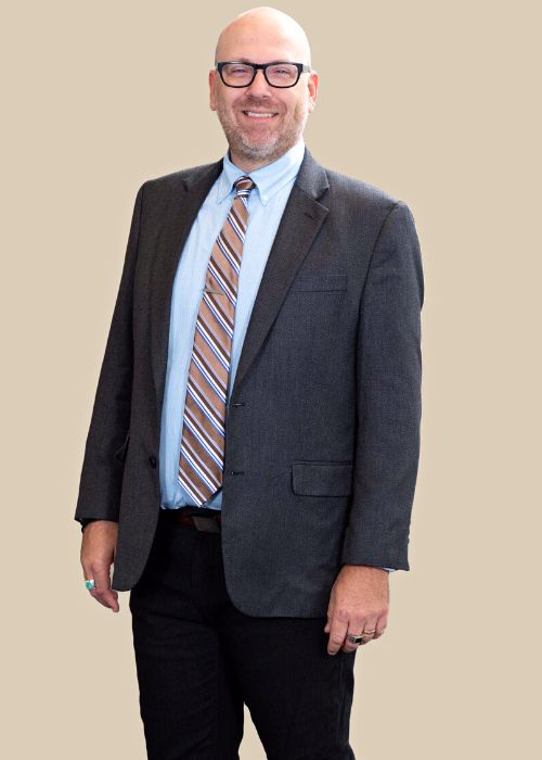 Zachary Holochwost stands confidently in a grey suit and blue striped tie, with a pleasant smile.