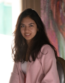 Smiling Peruvian marketing intern in a pink blazer, with abstract art in the background.